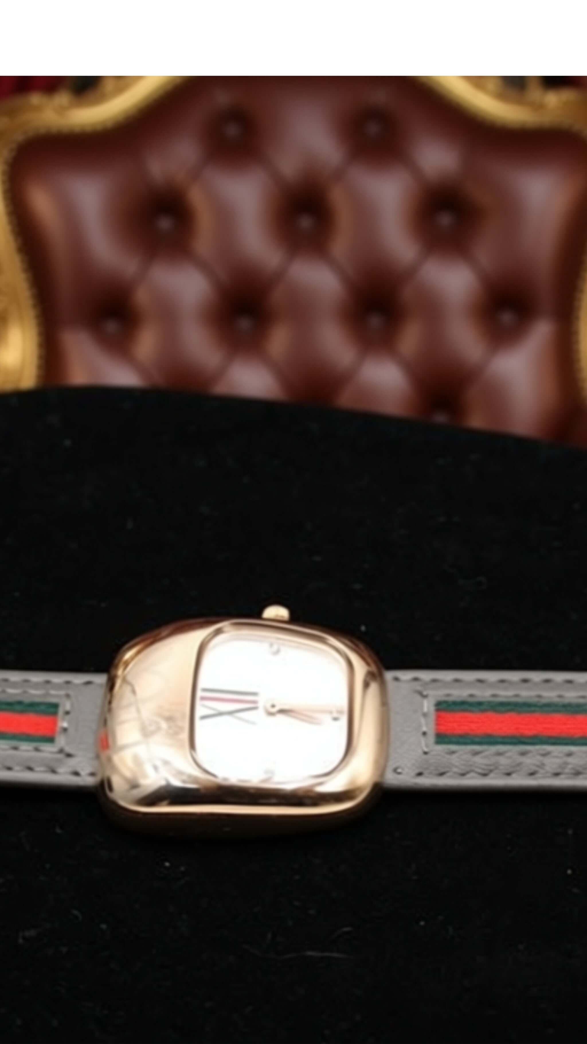 Luxury women's watch with a gold-tone case and grey strap featuring red and green stripes.